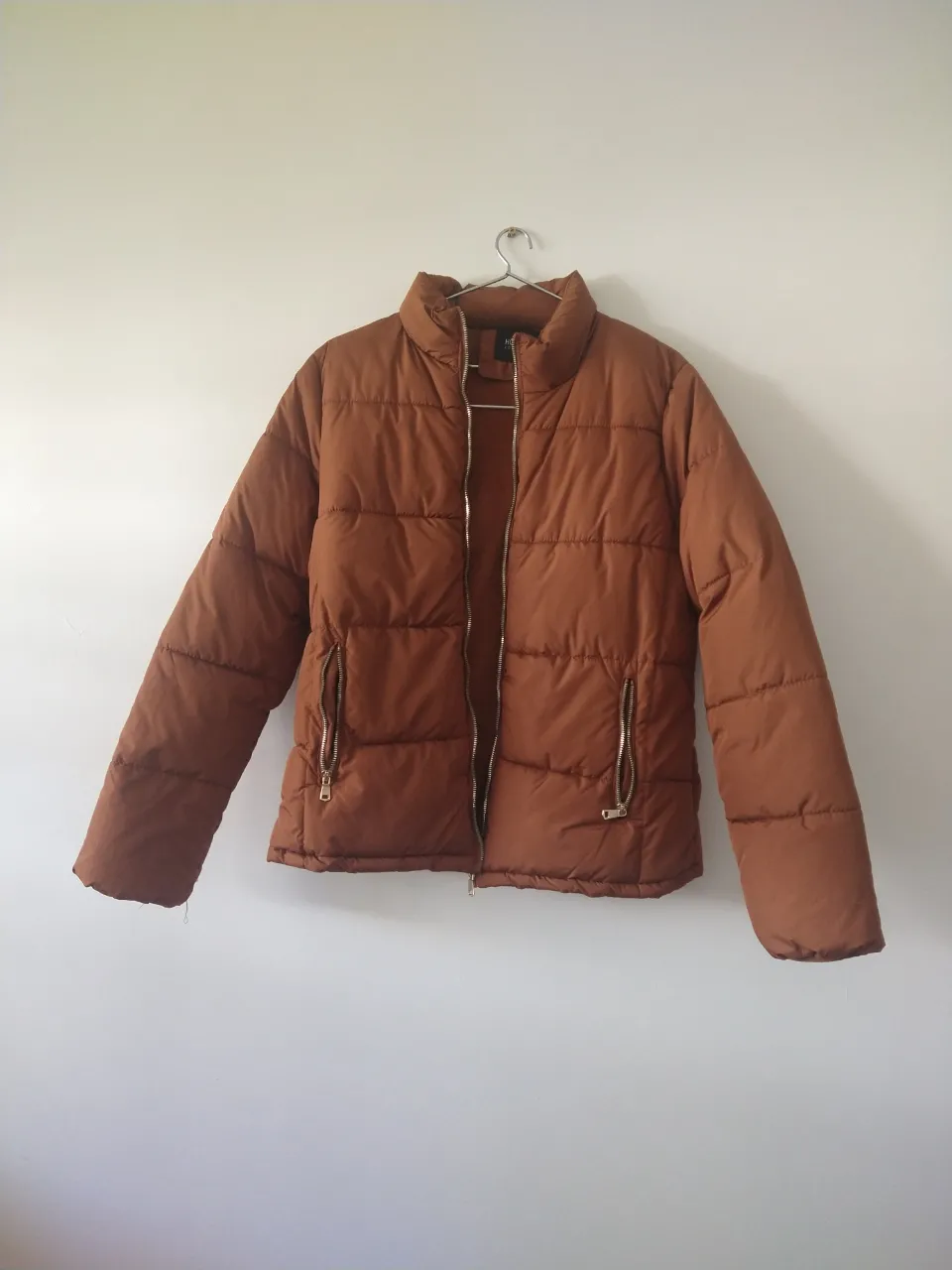 Campera acolchada marrón con cuello alto y cierre metálico. Posee bolsillos frontales con cierre.