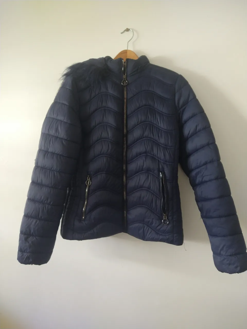 Campera azul marino acolchada con diseño de ondas, capucha con borde de pelo sintético desmontable y cierre delantero. Posee bolsillos laterales con cierre.