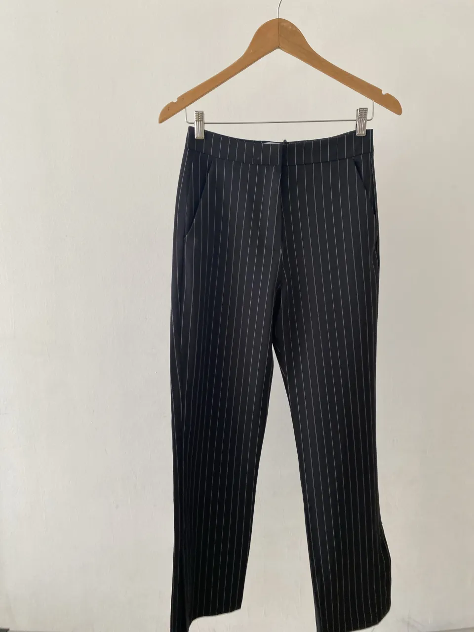 Pantalón de vestir tiro alto con rayas verticales finas blancas sobre fondo negro. Corte recto y moderno, ideal para un look elegante y sofisticado. Perfecto para la oficina o una salida formal.