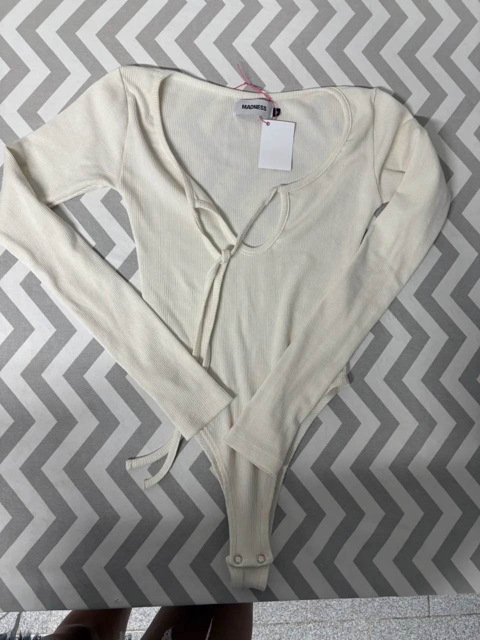 Body de manga larga color blanco roto, con escote en V y detalle de lazo en el frente. Posee broches en la parte inferior para mayor comodidad.