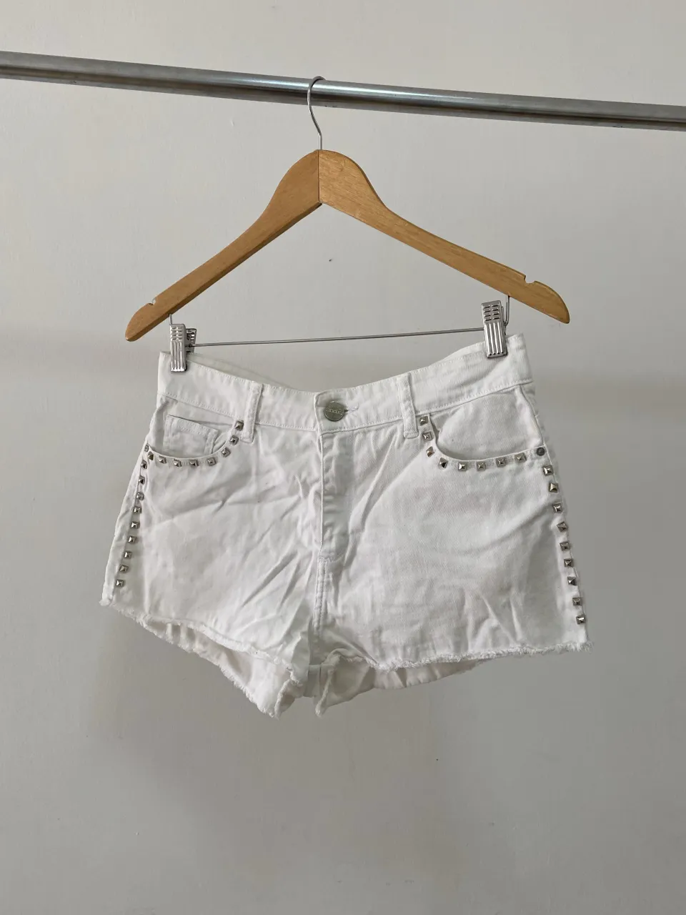 Shorts de jean blancos con tachas plateadas en los bolsillos y en los laterales. Tienen roturas deshilachadas en el borde inferior.
manchas en la foto  2. no se notan 