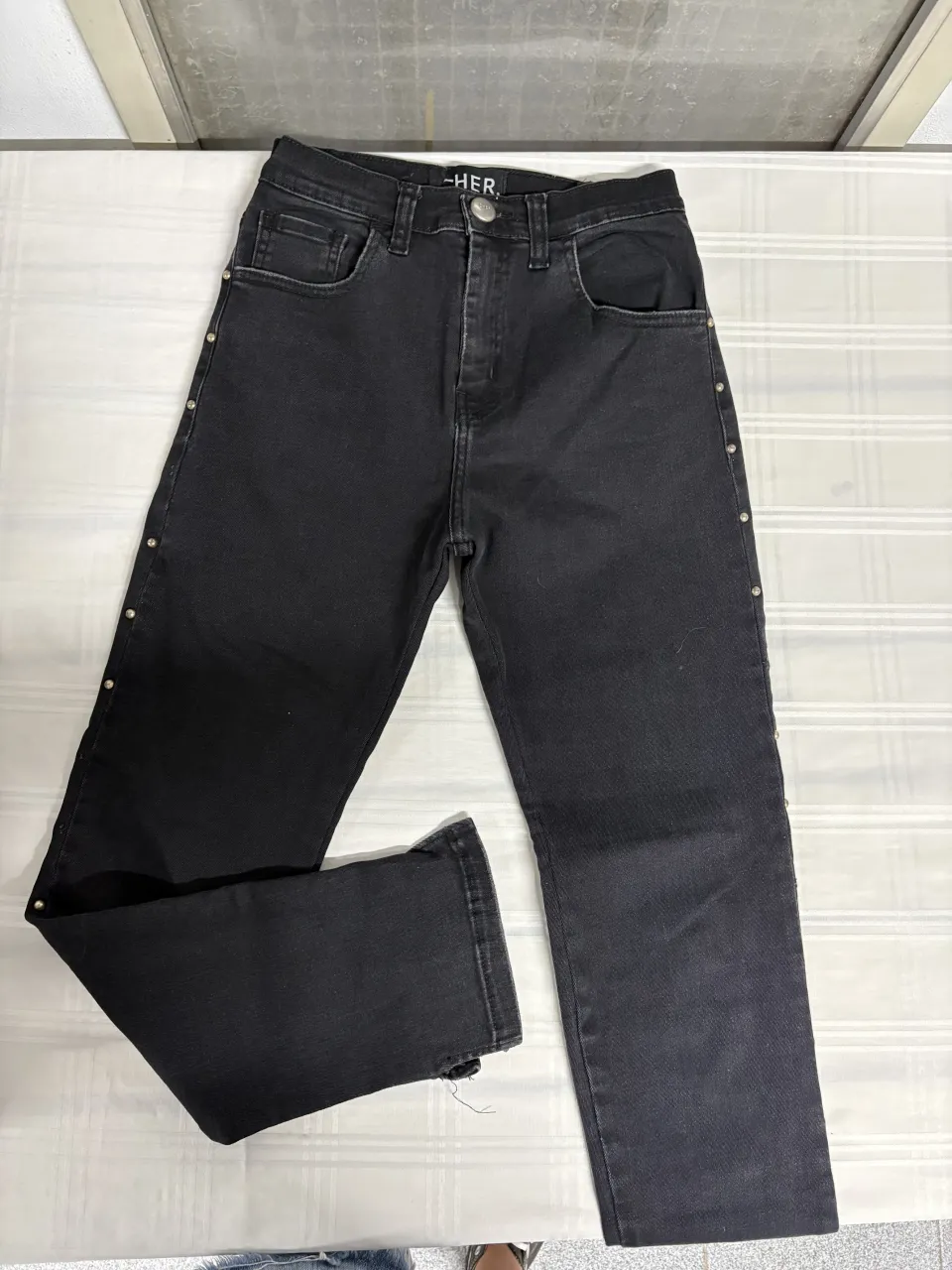 Jean negro tiro alto con tachas plateadas a los costados. Modelo recto con detalles desflecados en el bajo. Ideal para un look canchero y moderno.