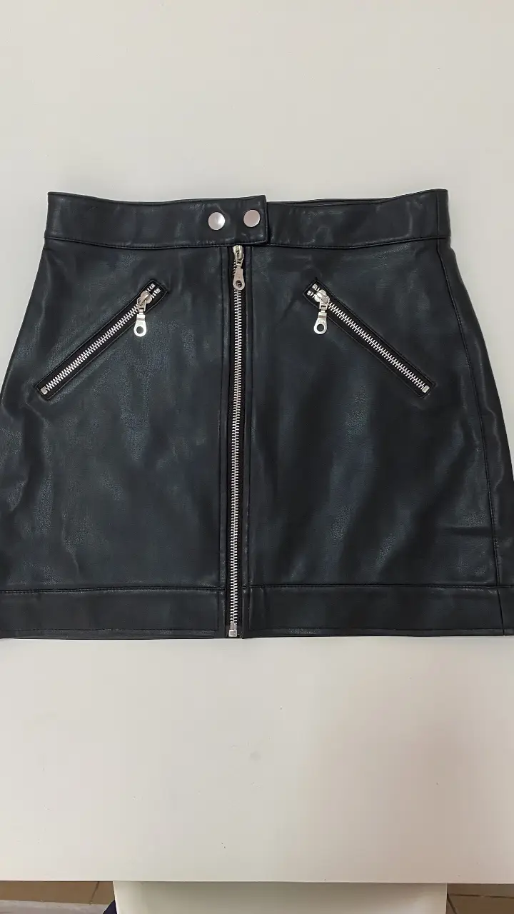 Pollera negra de cuero sintético con cierre y detalles de bolsillos con cierres. Talle S, ideal para un look rocker.