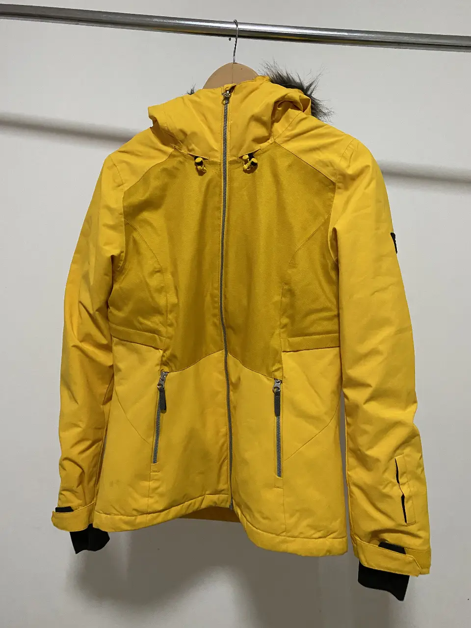 Campera de ski amarilla O'Neill para mujer, con capucha desmontable con borde de piel sintética, cierre frontal completo, múltiples bolsillos con cierre y logo de la marca en la manga. Ideal para la nieve y el frío.