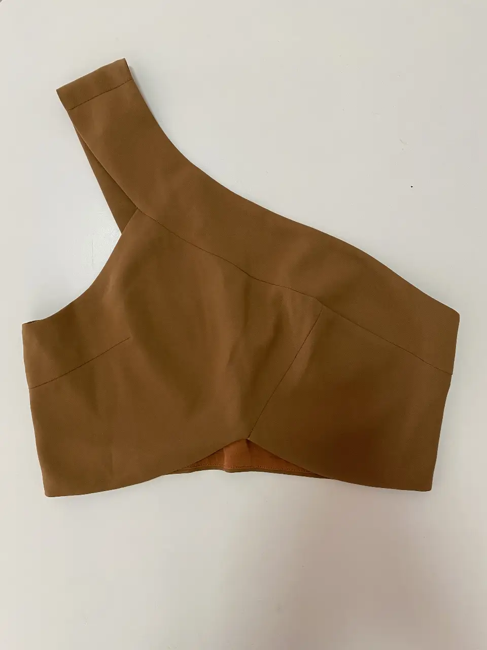 Top asimétrico de un solo hombro en color marrón. Ideal para un look moderno y sofisticado. Perfecto para combinar con pantalones de vestir o faldas.