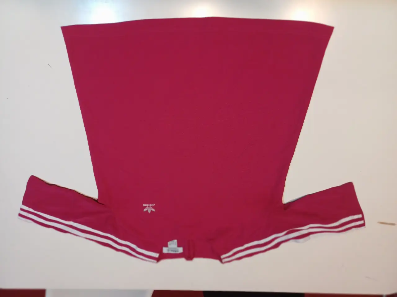Remera deportiva Adidas de color rojo, con detalles de las tres tiras blancas en las mangas. Ideal para actividades físicas o uso casual.