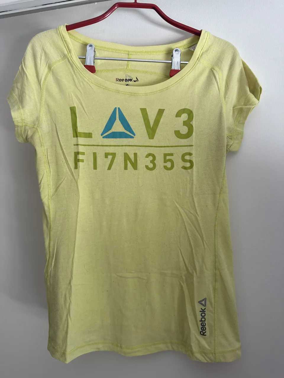 Remera deportiva amarilla de Reebok, con estampa "LAV3 F17N35S" en verde y azul. Ideal para entrenar o para un look casual y cómodo.