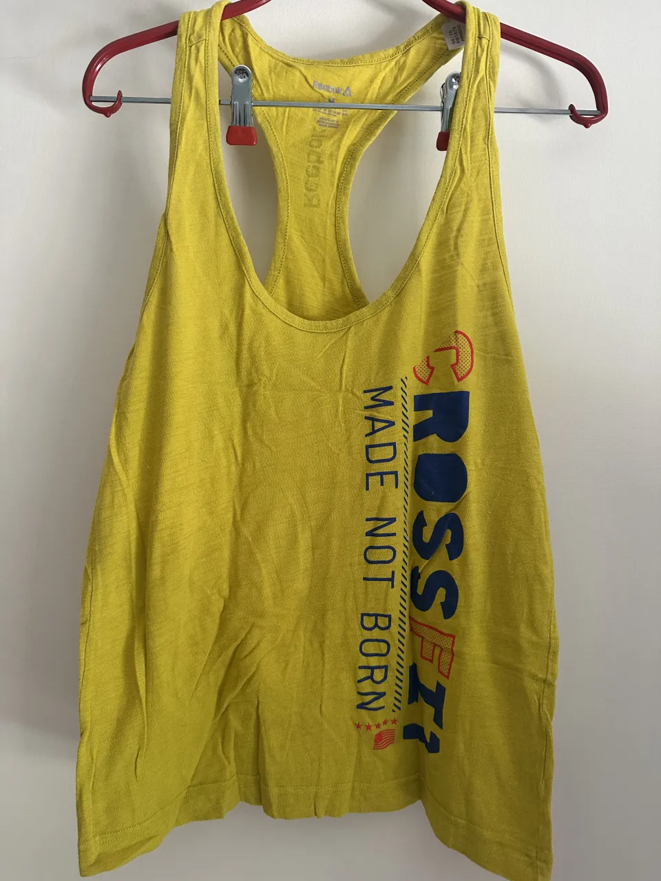 Musculosa deportiva amarilla de Reebok, con estampa "CROSSFIT MADE NOT BORN" en el frente. Ideal para entrenar o para un look casual y cómodo.