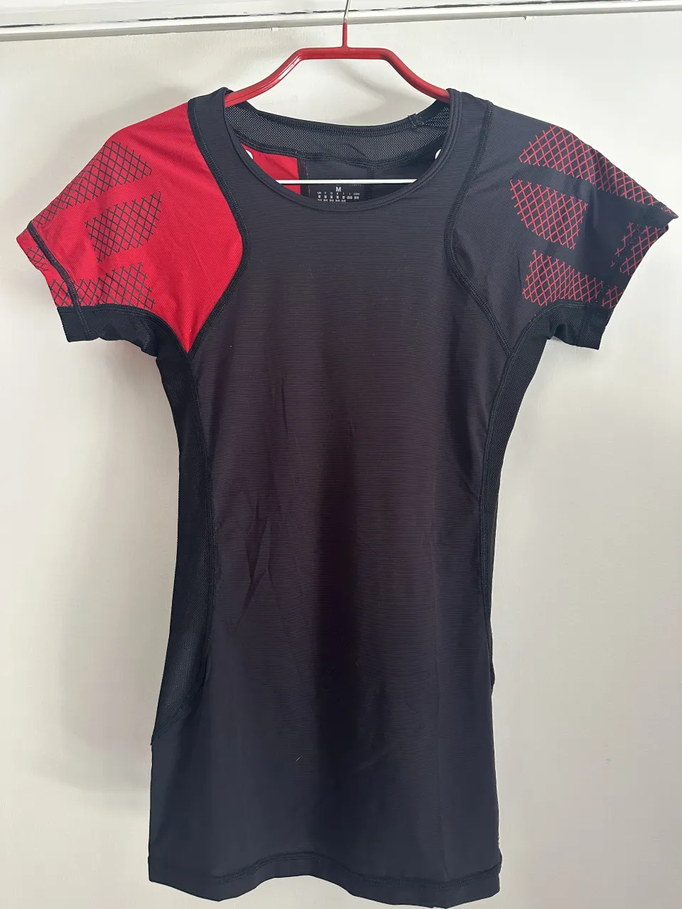 Remera deportiva negra con detalles en rojo en hombros y mangas. Ideal para entrenamientos intensos o actividades al aire libre. Diseño moderno y funcional. Reebok CrossFit