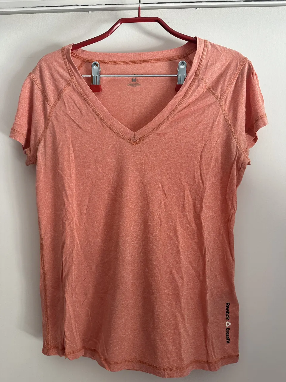 Remera deportiva talle M, color salmón, con cuello en V y mangas cortas. Ideal para entrenar o para un look casual y cómodo.