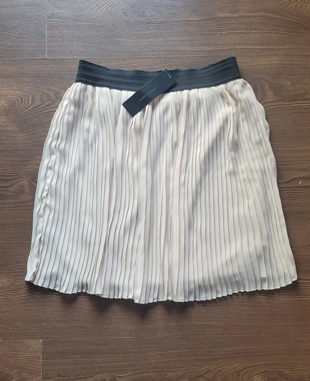 Pollera plisada de Cuesta Blanca con etiqueta, en color crudo con cintura elastizada negra. Ideal para un look elegante y versátil.