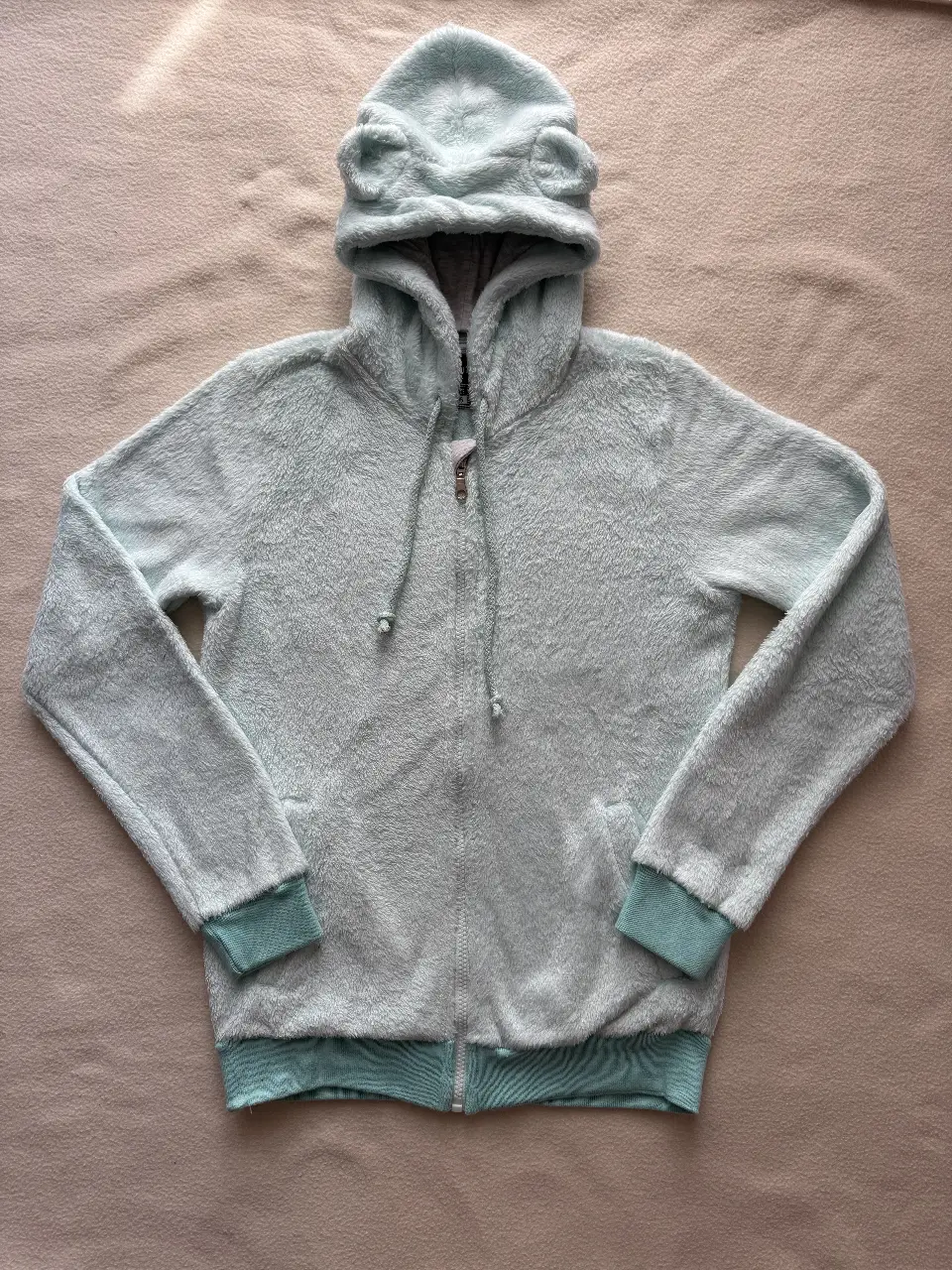 Buzo marca Buddies con cierre y capucha con orejitas color verde agua/celeste claro. Ideal para un look cómodo y divertido. Las medidas son: de largo tiene 59 cm, de ancho 44 cm y de largo de mangas 61 cm. En mi perfil pueden encontrar la misma campera en color rosa.