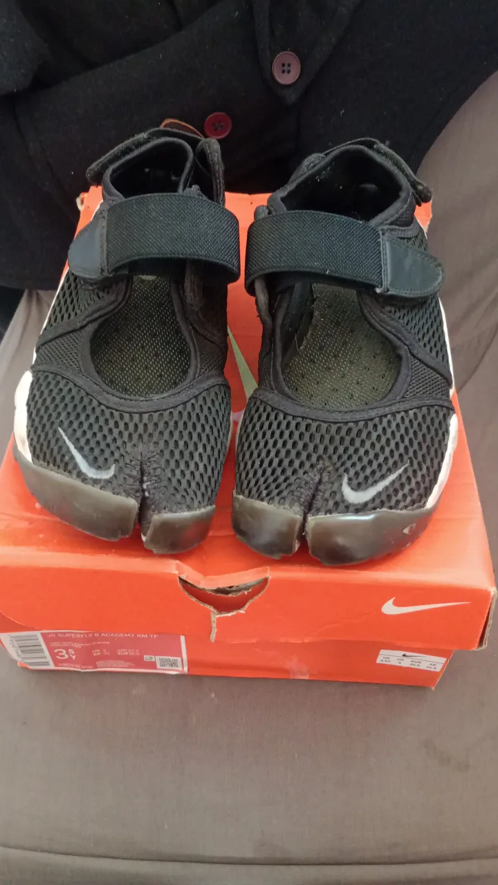 Zapatillas deportivas Nike negras con detalles blancos y suela transparente. Poseen abrojo para ajuste.