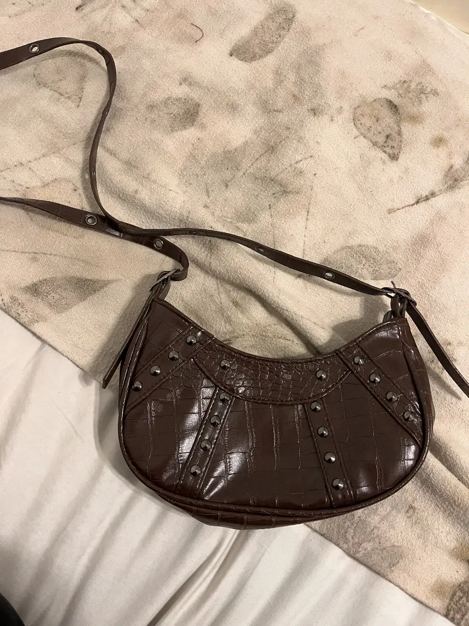 Cartera bandolera marrón con diseño de cocodrilo y tachas. Ideal para un look moderno y canchero.