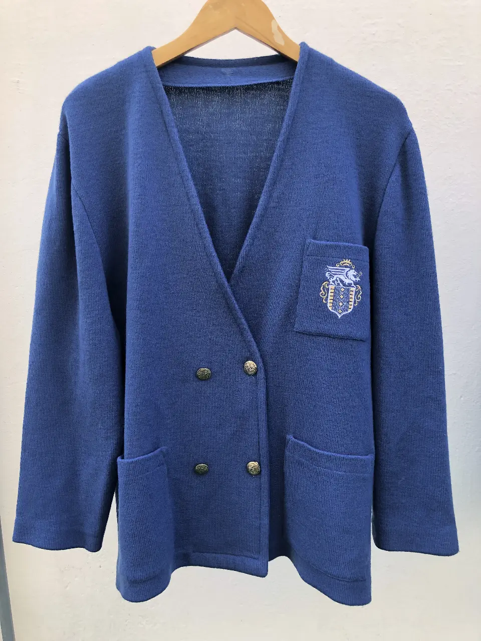 Cardigan azul con botones dorados y un bordado en el bolsillo. Ideal para un look elegante y vintage.