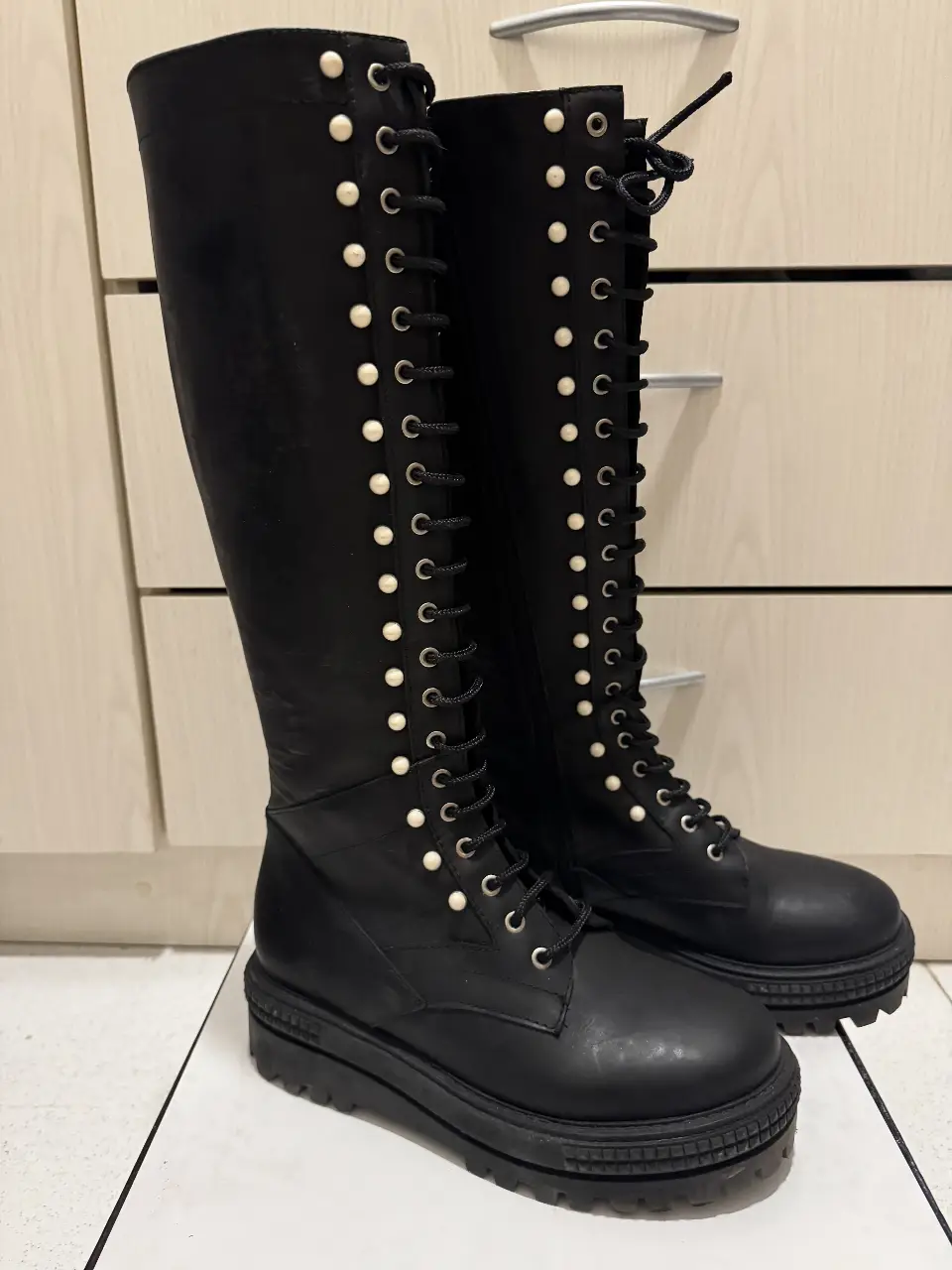 Botas altas negras con cordones y detalles de perlas. Diseño moderno y elegante, ideales para un look audaz y sofisticado. Perfectas para combinar con diferentes outfits.