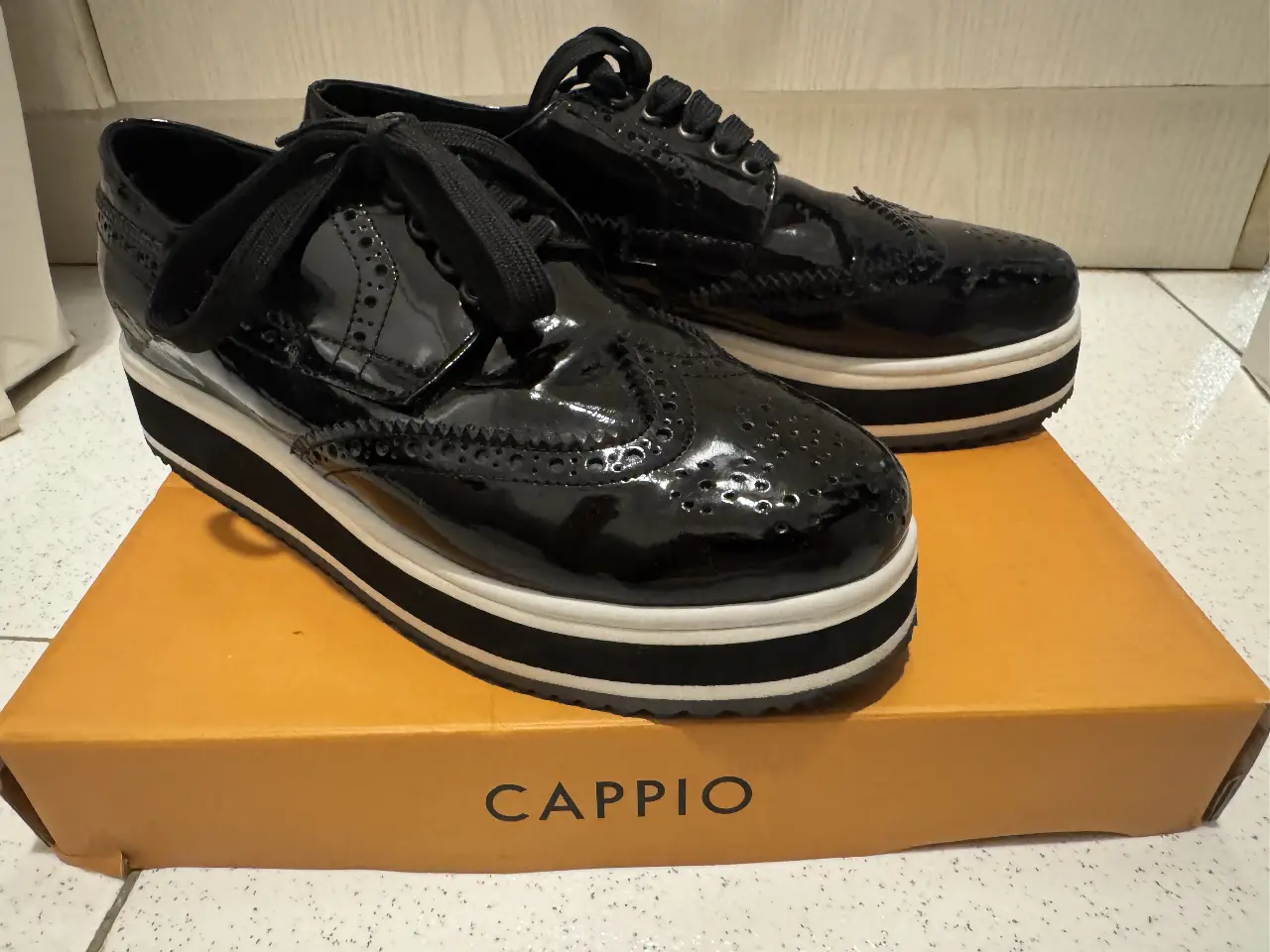 Zapatos de plataforma negros charol con detalles brogue y suela blanca. Talle 39, de la marca Cappio. Ideales para un look elegante y moderno.