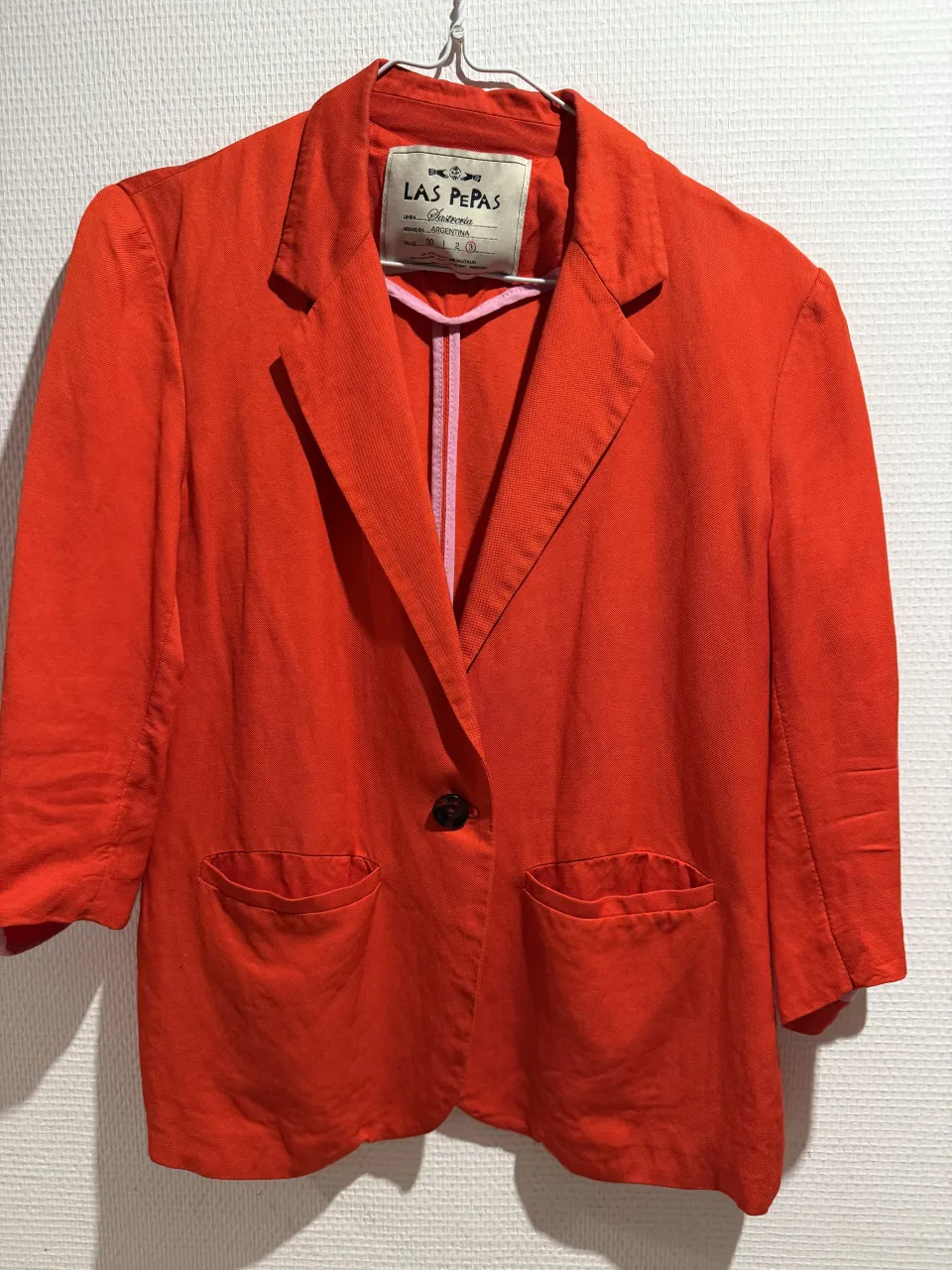 Blazer naranja de lino, ideal para un look canchero y moderno. Tiene mangas 3/4 y un solo botón al frente. Los bolsillos le dan un toque práctico y con estilo.