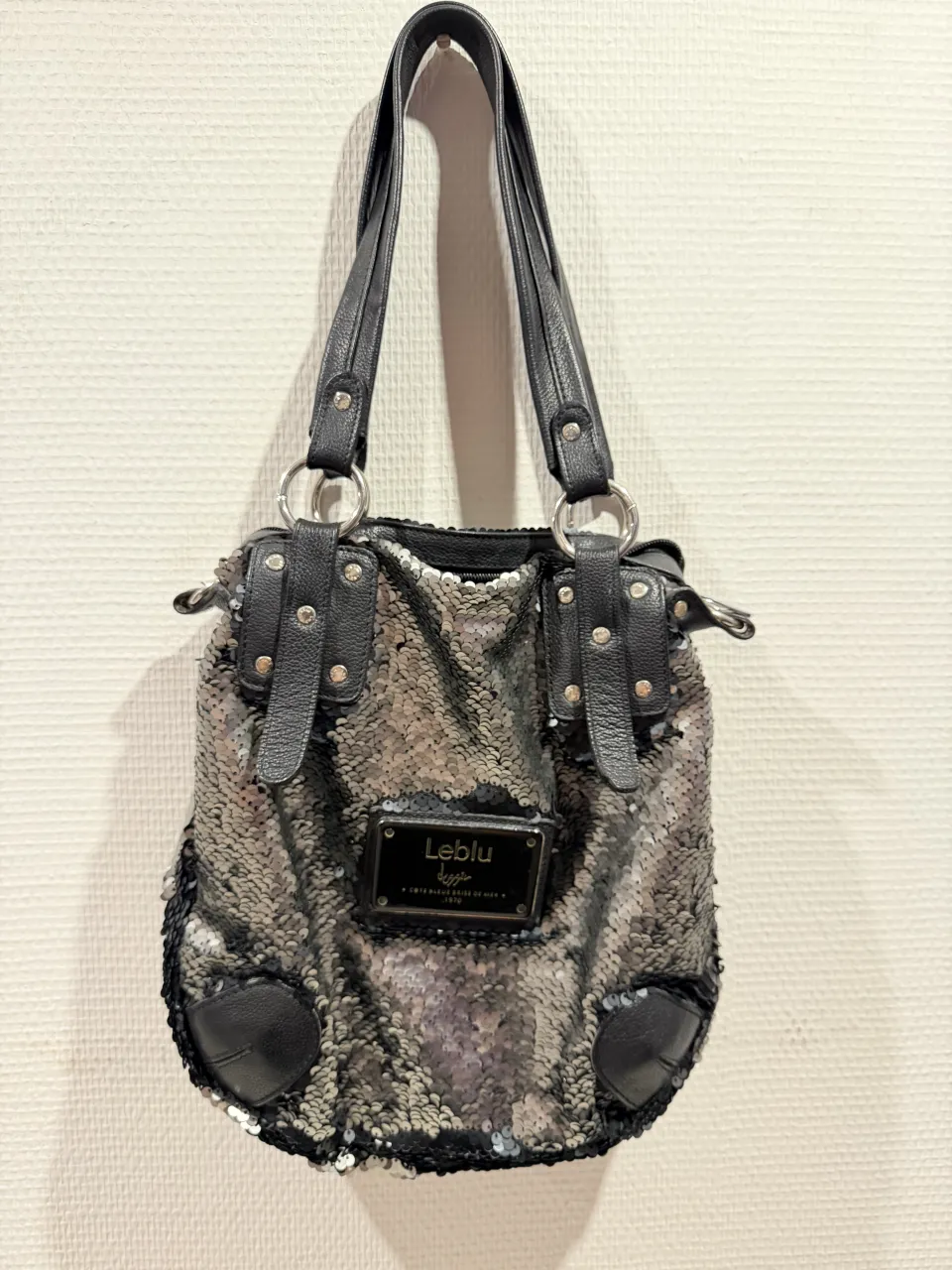 Bolso plateado con lentejuelas y detalles en cuero negro. Ideal para darle un toque de brillo a tus looks de noche o para un evento especial. Tiene correa desmontable y es súper espacioso.