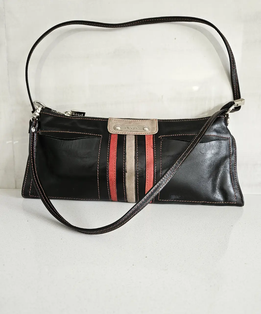 Cartera bandolera de cuero negro con detalles en rojo y beige. Ideal para un look casual y elegante.