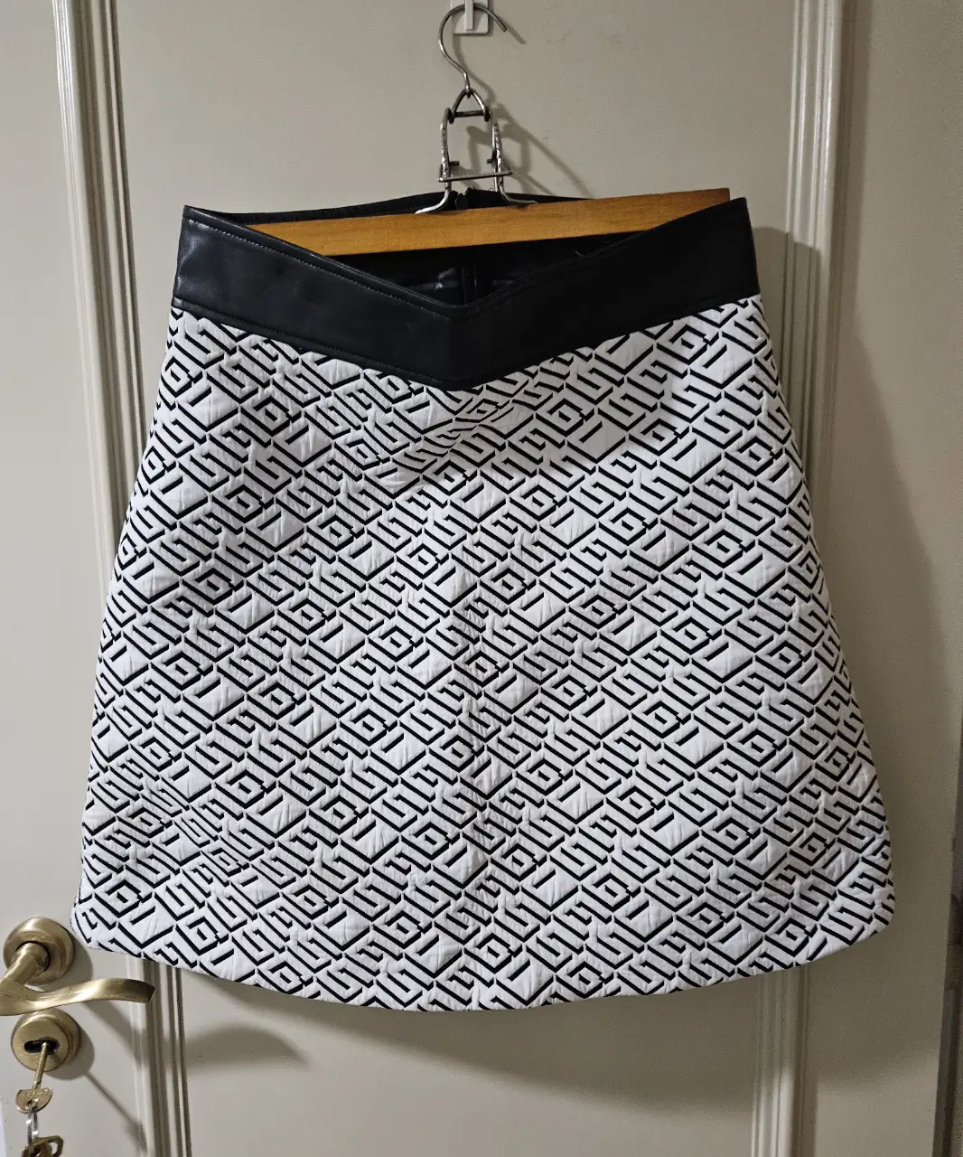 Pollera Guess con diseño geométrico en blanco y negro, con detalle de cuero sintético en la cintura. Ideal para un look elegante y moderno.