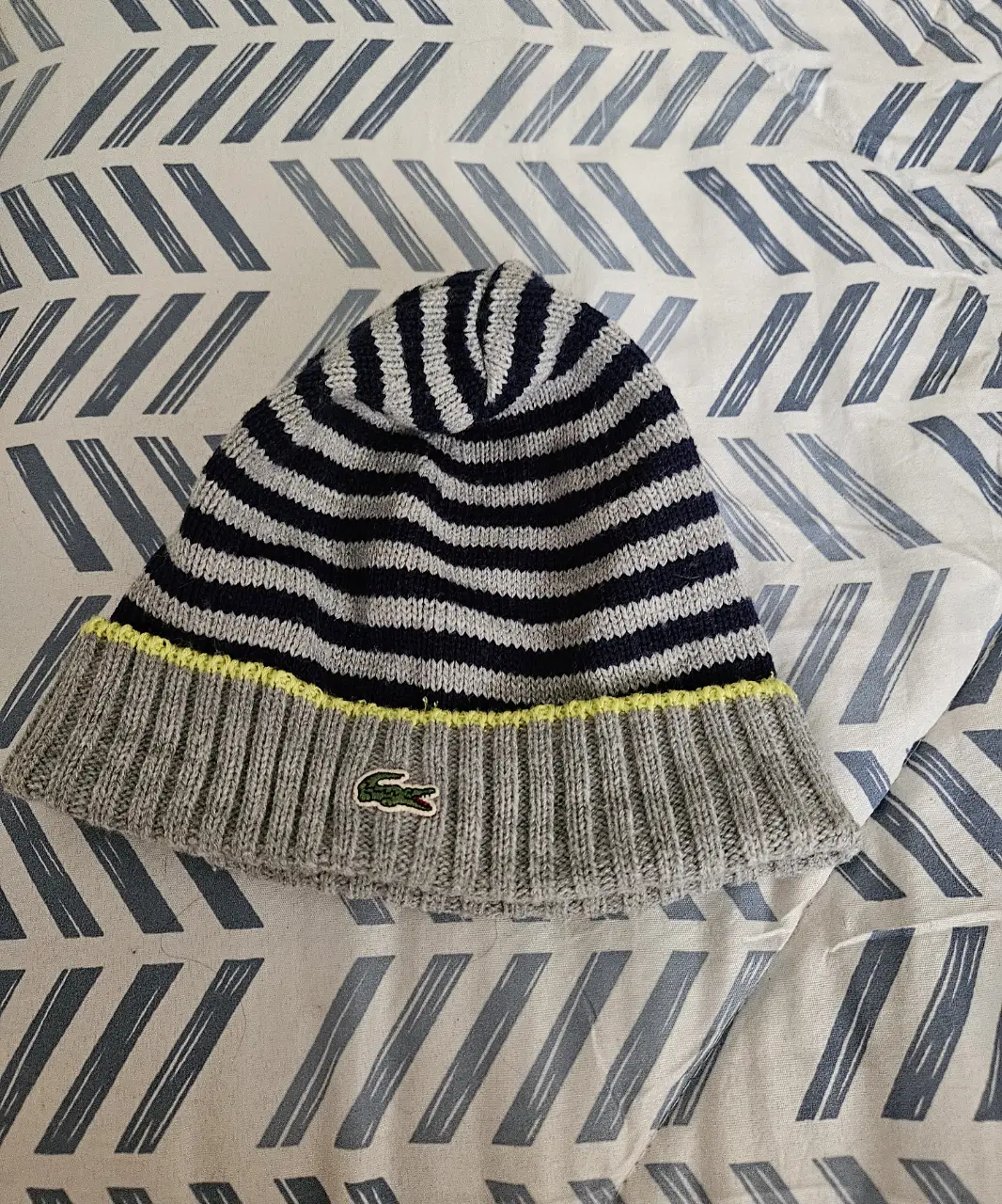 Gorro tejido a rayas en gris y azul marino con detalle amarillo y logo de la marca. Ideal para el invierno.