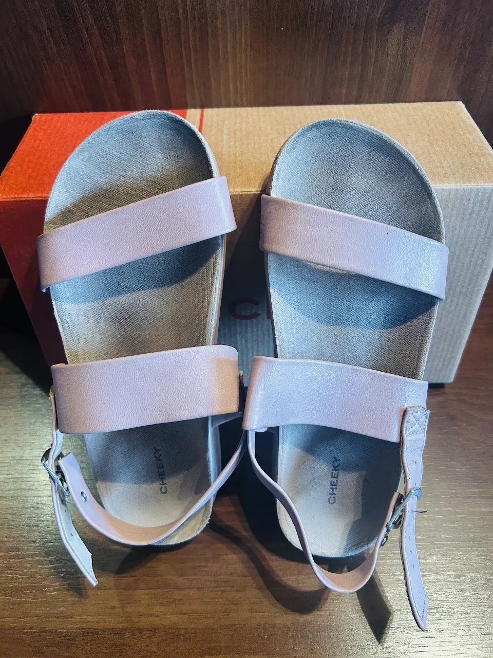 Sandalias bajas color rosa pálido, con dos tiras anchas sobre el empeine y una tira fina que se ajusta al tobillo con hebilla. Ideales para el verano y para un look casual.