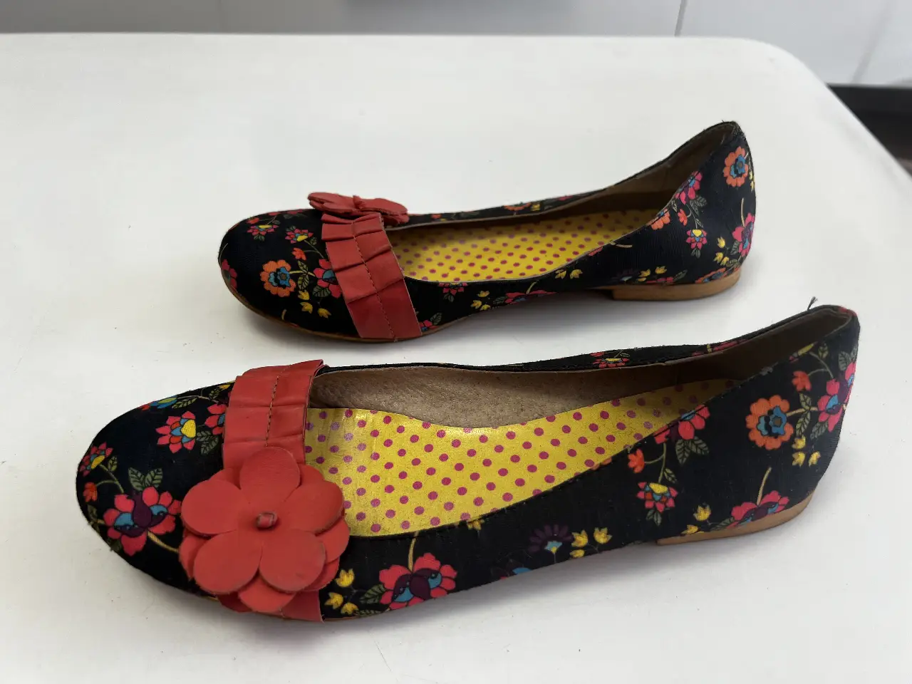 Ballerinas de mujer con estampado floral en negro, detalles en rojo y plantilla amarilla con lunares. Ideales para un look casual y femenino.