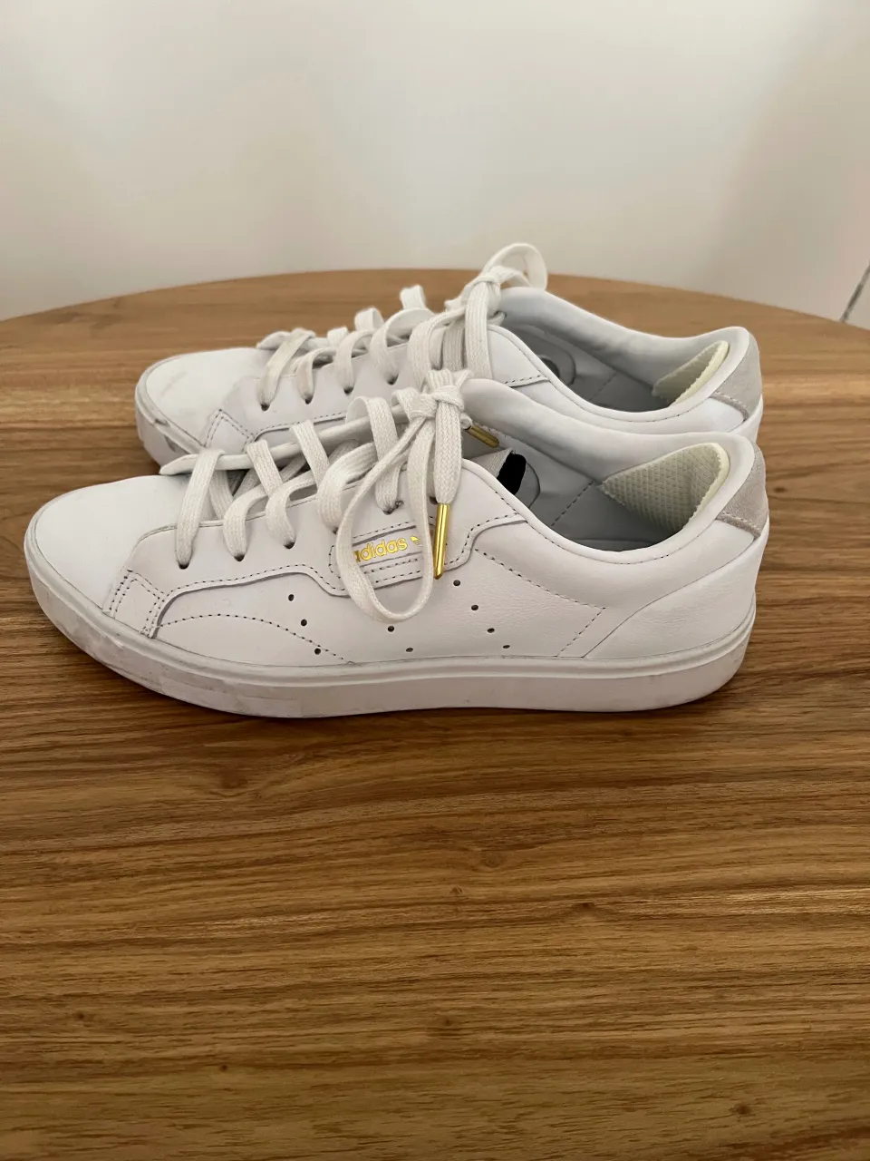 Zapatillas blancas de cuero con detalles dorados en los cordones y en el logo de la marca.