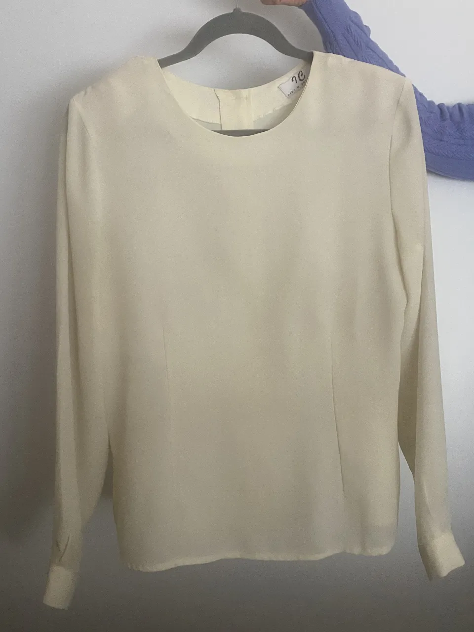 Blusa de seda color crema, con mangas largas y botones en la espalda. Un clásico atemporal con hombreras, ideal para un look elegante y sofisticado.