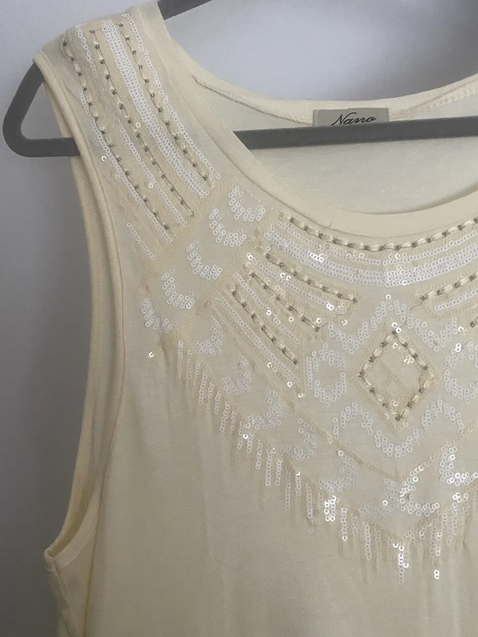 Musculosa de color amarillo pálido con detalles de lentejuelas y canutillos bordados en el escote, con un diseño geométrico que le dan un toque boho chic. Ideal para un look de verano o para una salida informal.