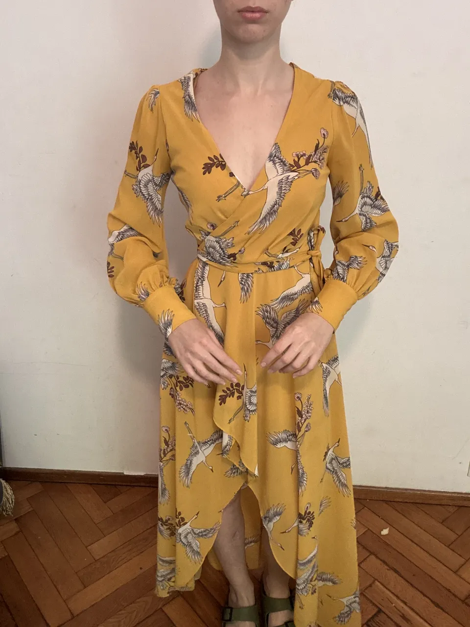 Vestido largo amarillo con estampa de grullas y flores. Diseño cruzado con escote en V, mangas largas y detalle de volados en la falda. Ideal para un look elegante y bohemio.