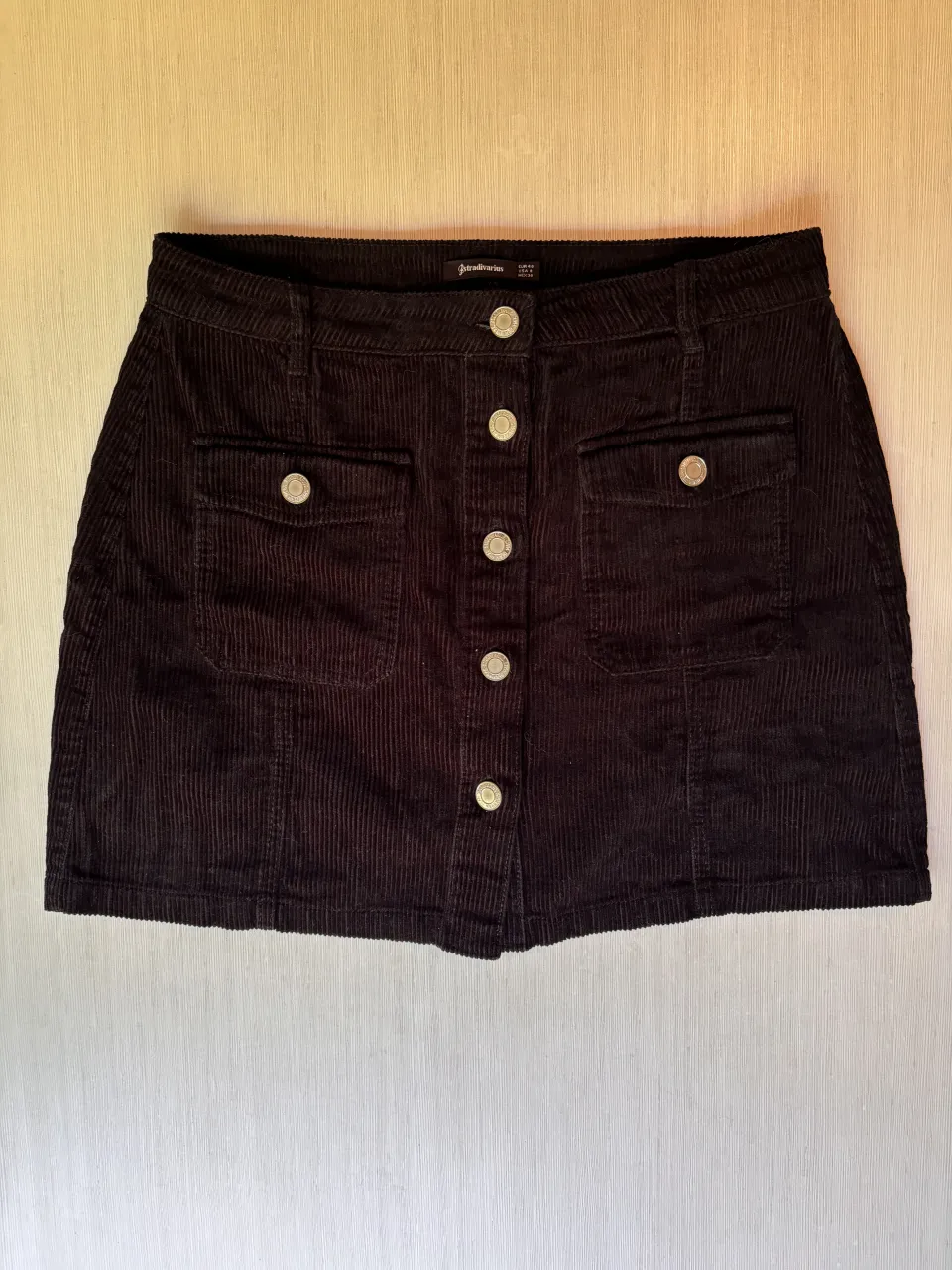 Pollera de pana negra, tiro alto, con botones al frente y bolsillos. 