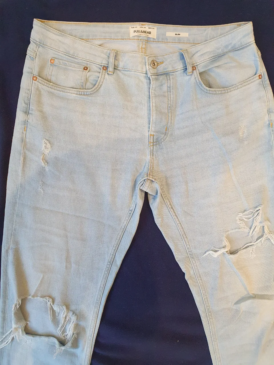 Jeans de hombre Pull&Bear celeste claro, con roturas en las rodillas. Corte slim pero bastante ancho, ideal para un look casual y moderno. Perfecto para combinar con remeras y zapatillas.
