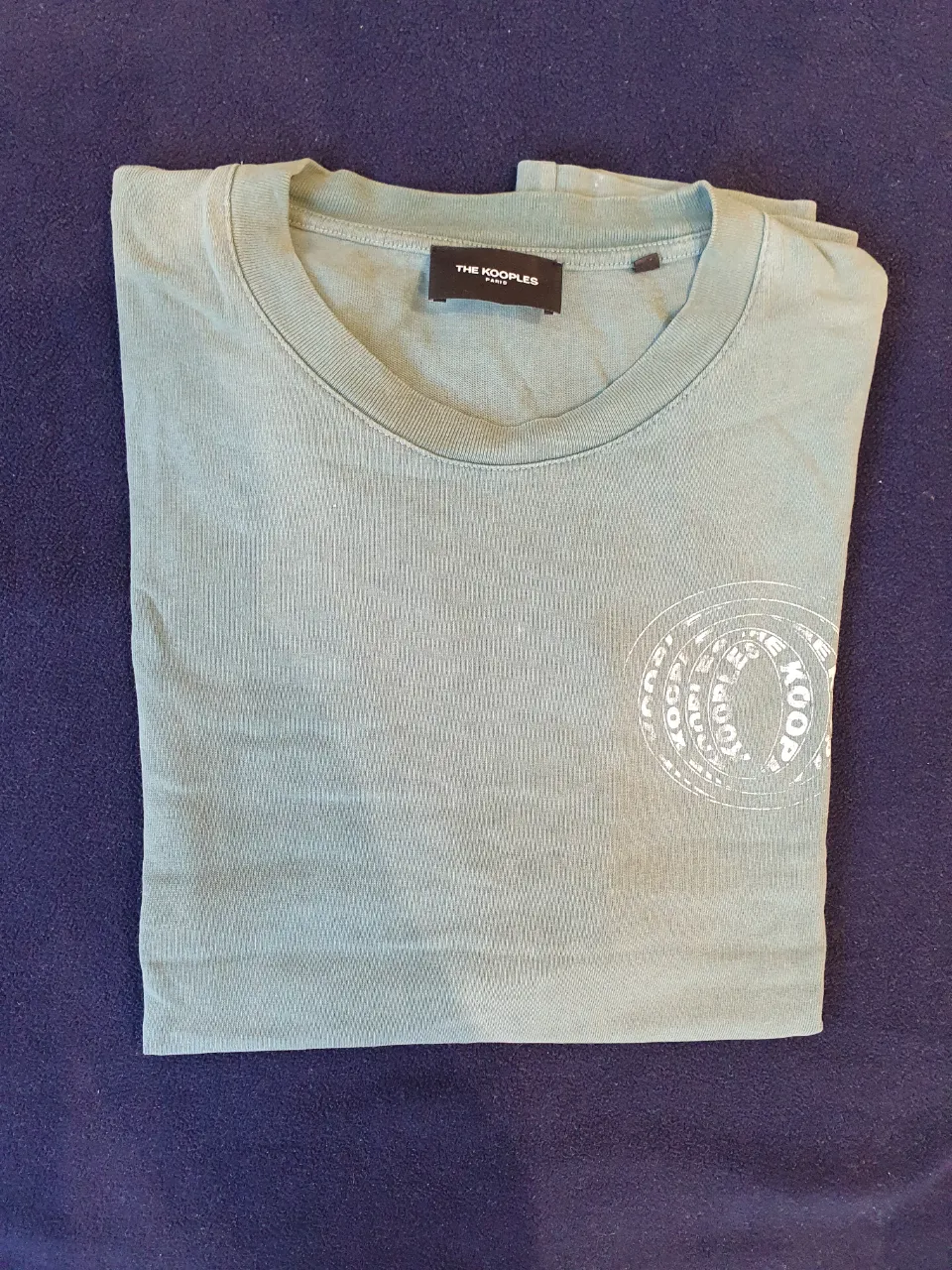 Remera de hombre The Kooples, manga corta, color verde agua, con estampado en el frente y detalles de la marca. Ideal para un look casual y moderno.