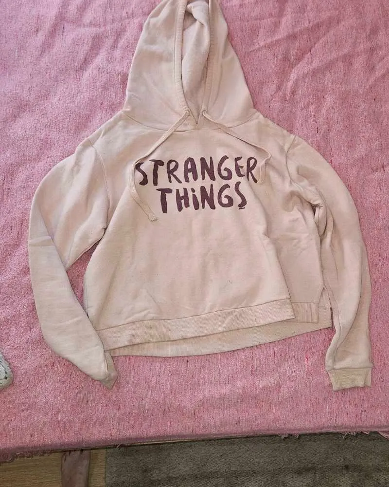 Hoodie rosa pálido con estampa "Stranger Things" en el frente. Diseño moderno y cómodo, ideal para un look casual y relajado. Perfecto para los fans de la serie.