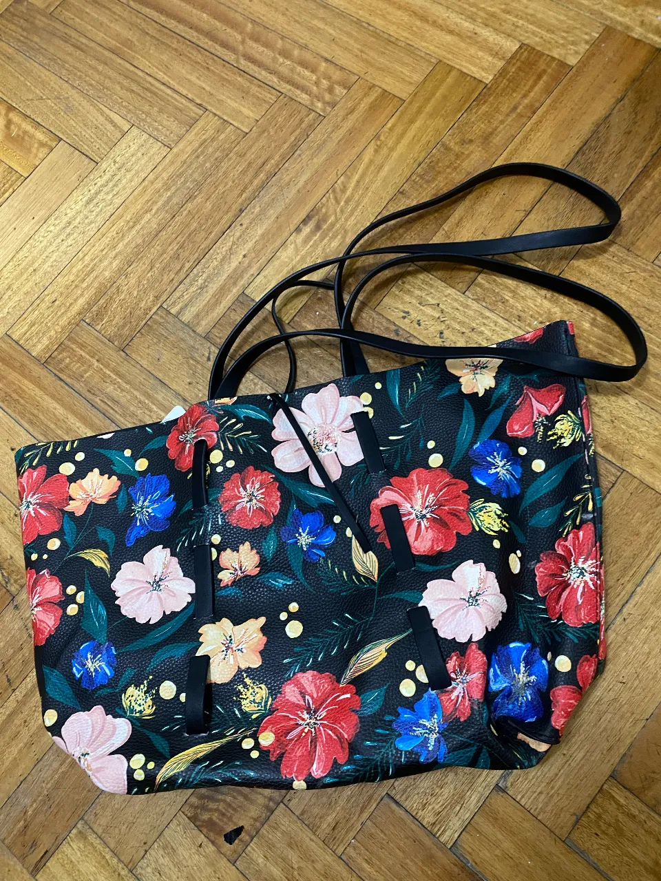 Bolso tote negro con estampa floral vibrante. Ideal para el día a día, para llevar todo lo que necesitás con mucho estilo. Su diseño reversible lo hace súper versátil.
