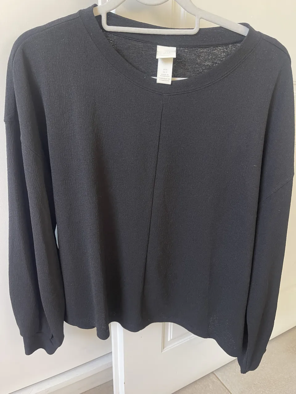 Remera negra de manga larga con cuello redondo. Posee una costura central vertical en el frente.