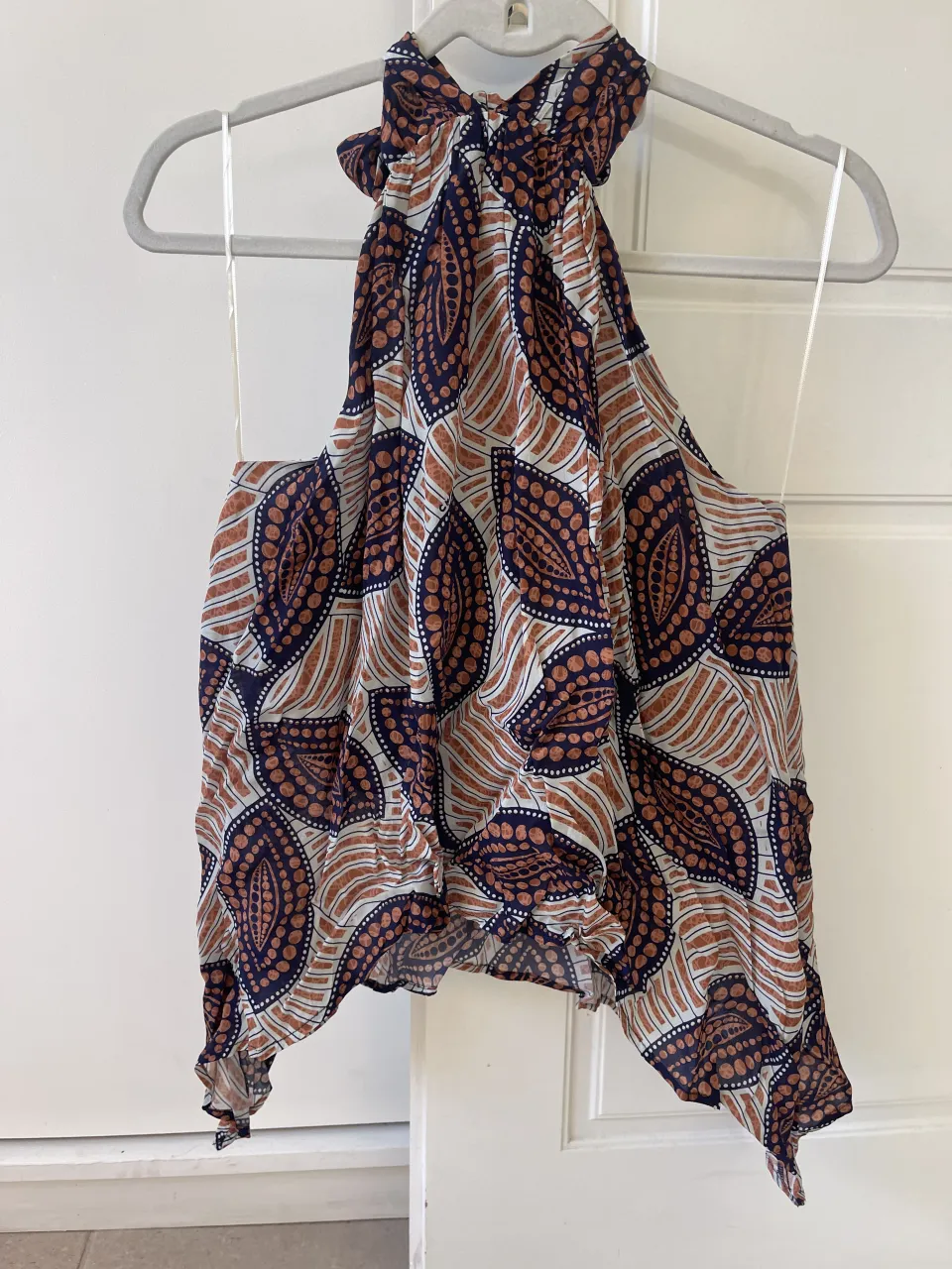 Top estampado con cuello halter y lazo en la nuca. Posee un estampado de hojas y círculos en tonos azul marino, naranja y blanco.