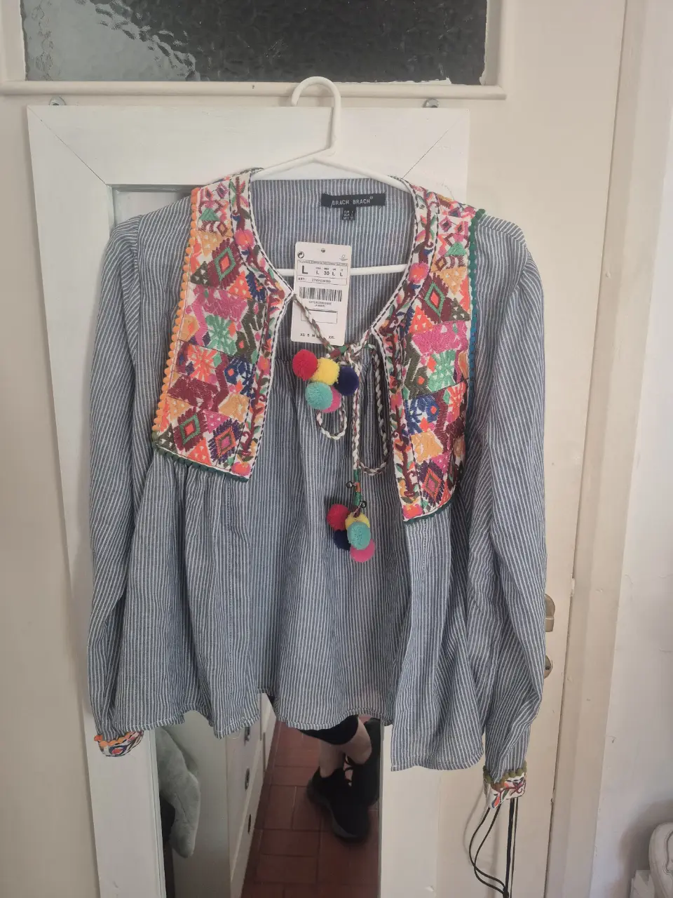 Blusa de mujer estilo boho con bordados coloridos en el frente y mangas largas. Detalles de pompones y rayas verticales. Ideal para un look casual y con onda.