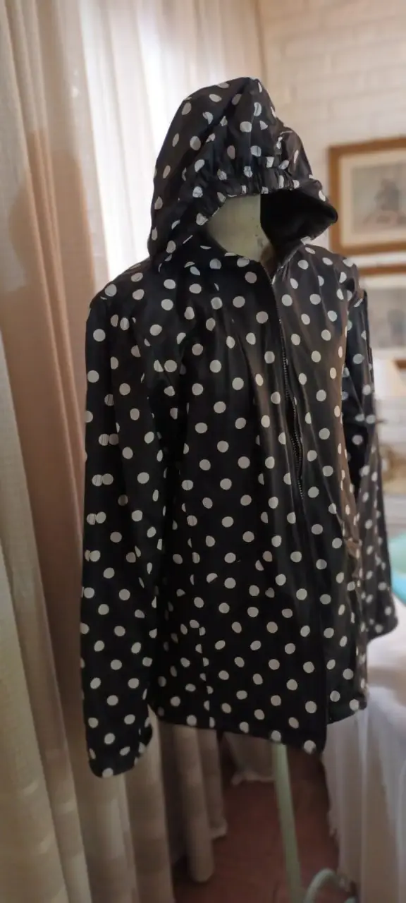 Impermeable con capucha y lunares blancos sobre fondo negro. Cierre frontal y diseño clásico.