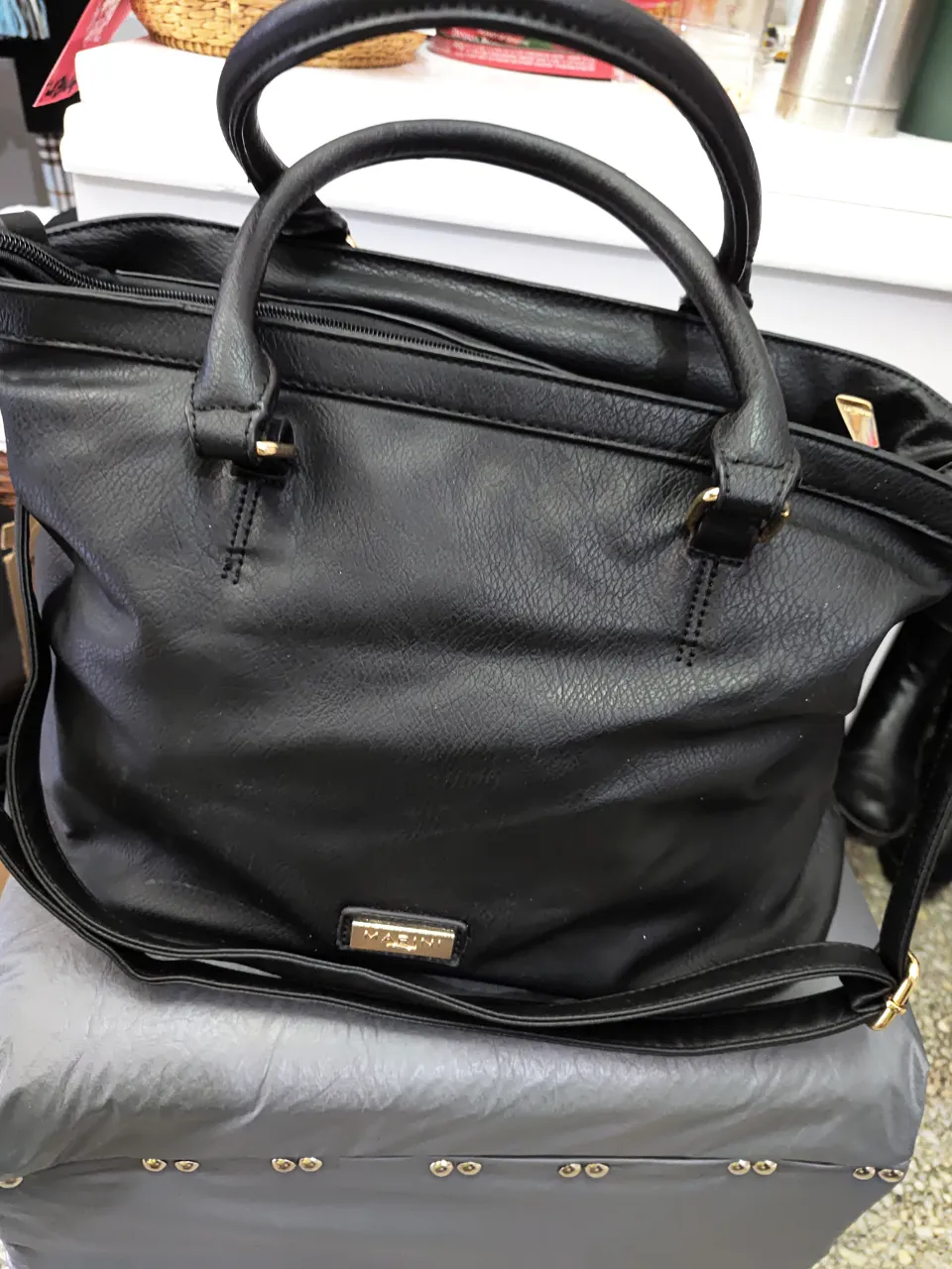 Cartera negra de hombro, con manijas y correa ajustable. Posee un bolsillo interno con cierre y detalles dorados. Ideal para uso diario. 
Tamaño mediano.
