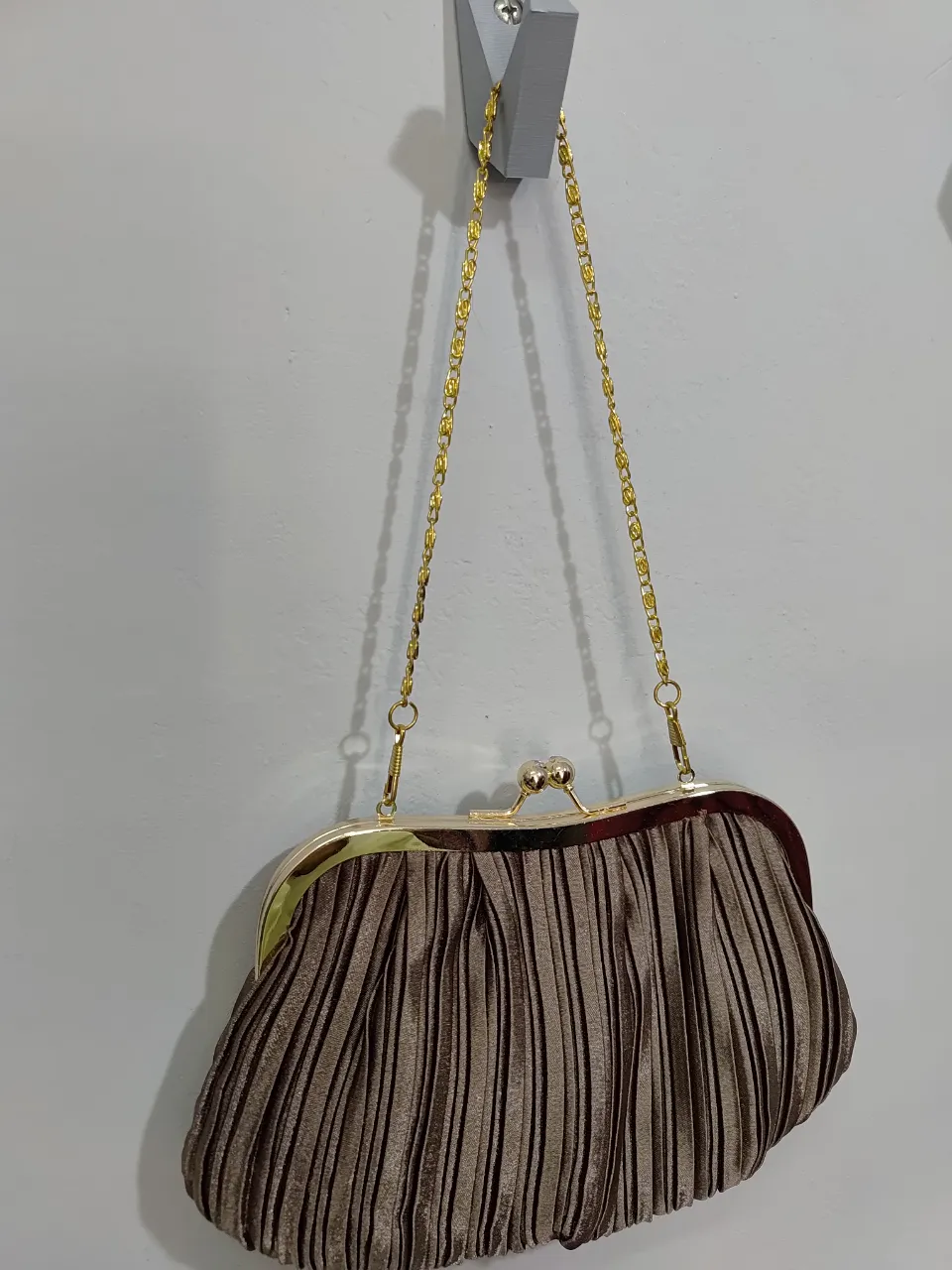 Cartera de mano vintage, color marrón con detalles dorados. Diseño plisado y cadena dorada para colgar. Ideal para eventos formales o fiestas.
Marca ISADORA