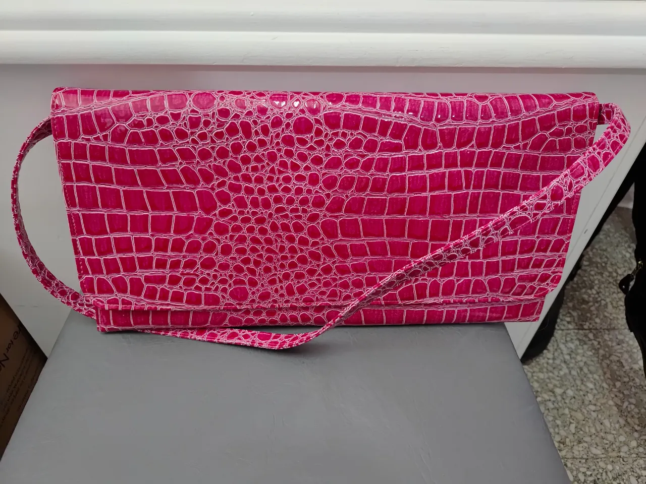 Cartera de mano fucsia con textura de reptil. Ideal para eventos y salidas nocturnas. Incluye correa para usar al hombro. Medida 38cm x 18cm