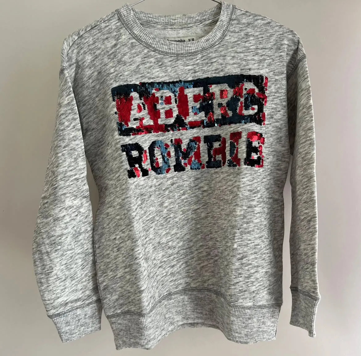 Buzo de cuello redondo Abercrombie & Fitch para niña, de color gris jaspeado con estampado del logo de la marca en lentejuelas rojas y azules.
Talle 9/10 
Busto: 46
Brazo: 46
Largo: 58
