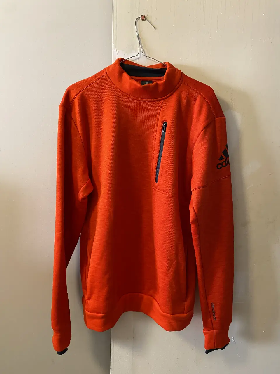 Buzo deportivo Adidas naranja con cuello alto y cierre en el pecho. Ideal para actividades al aire libre o para un look casual y cómodo.