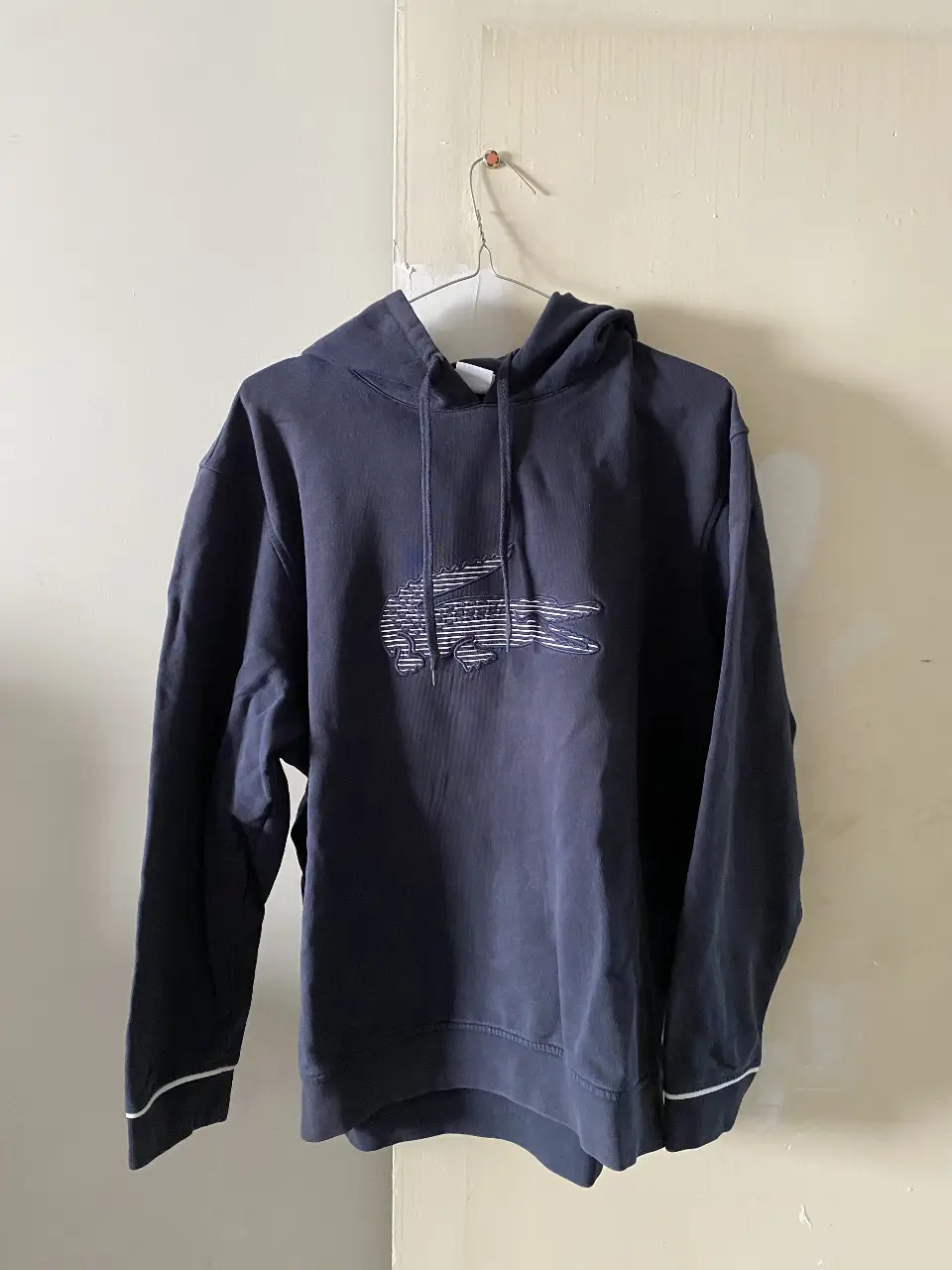 Buzo con capucha de hombre, azul marino con logo de Lacoste bordado en blanco. Detalles de ribete blanco en los puños. Talle 7.