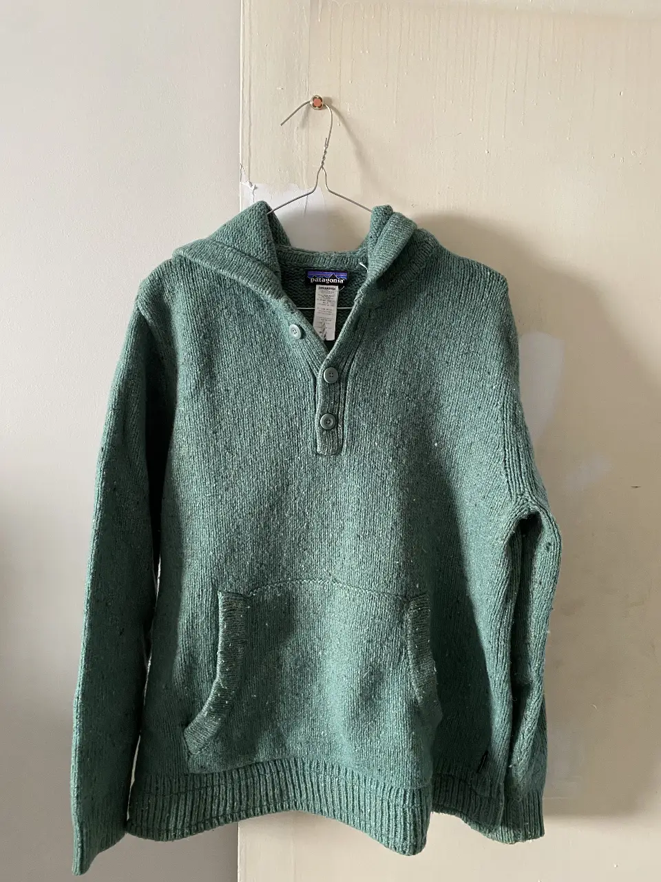Sweater Patagonia verde con capucha y bolsillo frontal. Diseño clásico con botones en el cuello. Ideal para un look casual y abrigado.