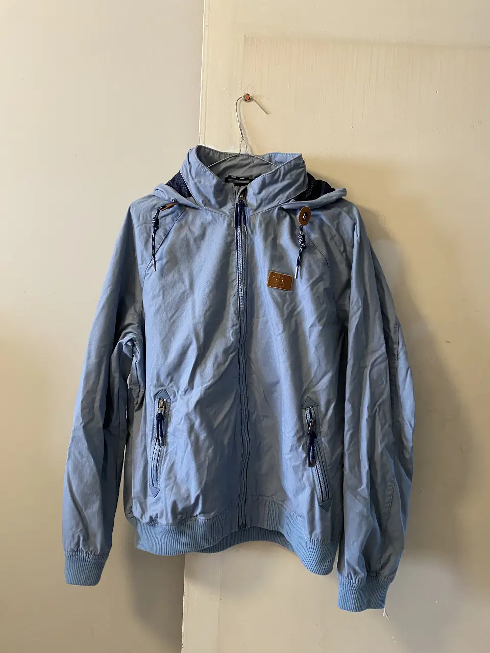 Campera rompevientos celeste con capucha y cierre. Ideal para usar en días frescos. Posee bolsillos con cierre y detalles en azul marino. Marca Springfield. talle 44