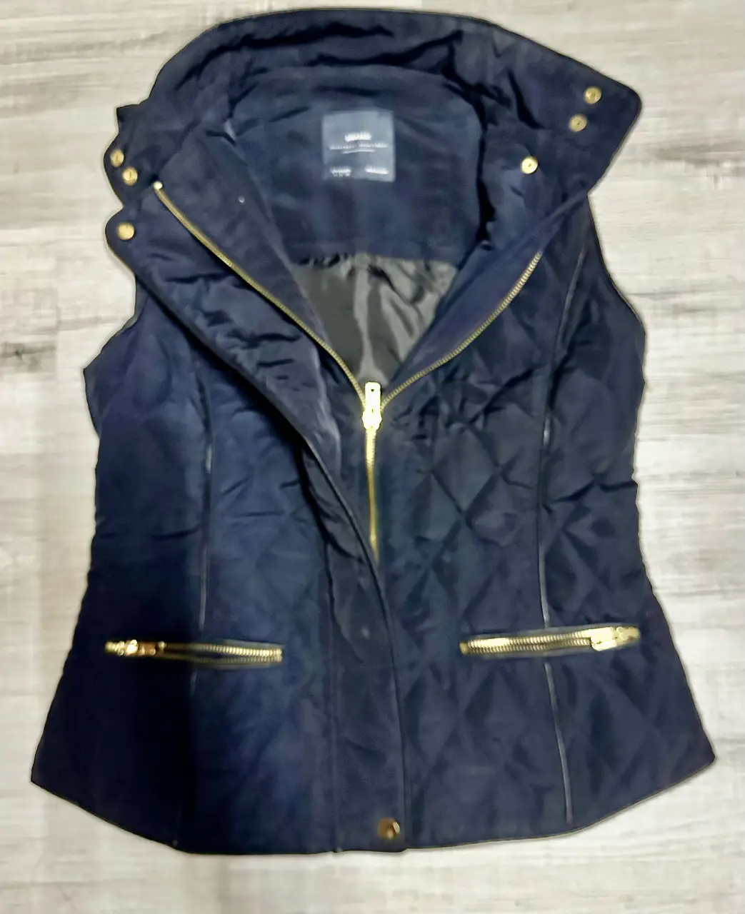 Chaleco acolchado de mujer, azul marino con detalles dorados. Ideal para un look casual y abrigado. Cuenta con cierre y bolsillos con cremalleras doradas. Perfecto para el invierno.